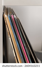 Vertical stack of colorful vinyl record sleeves on a white shelf