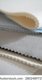Vertical stack of fabric samples in white, blue, grey and black. Zigzag cut edges highlight woven texture. Textile material options for garment production.                