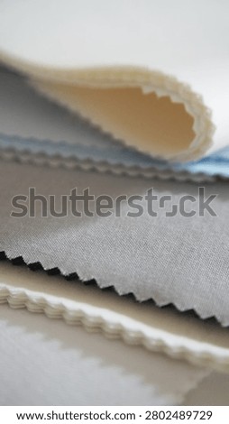 Vertical stack of fabric samples in white, blue, grey and black. Zigzag cut edges highlight woven texture. Textile material options for garment production.                