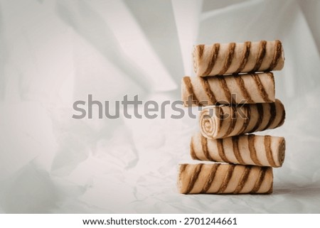 A vertical stack of five golden brown wafer rolls with distinct chocolate swirls against a softly textured white backdrop.