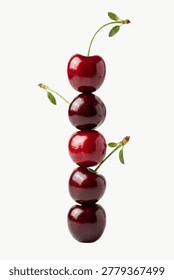 A vertical stack of five ripe red cherries balanced against a white background