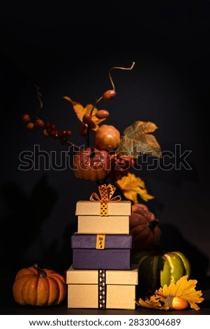 Vertical stack of gift boxes with pumpkins berries and autumn leaves on black background for Halloween Thanksgiving promotion
