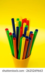 Vertical stack of plastic straws representing beverage accessories and playful summer themes, Colorful Beverage Straws Grouped in Yellow Cup with Isolated Background