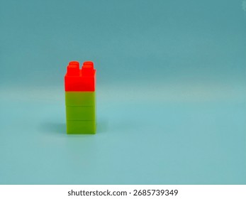 Vertical stack of red and green toy building blocks on blue background.

