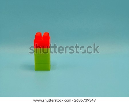Vertical stack of red and green toy building blocks on blue background.
