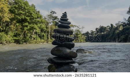A vertical stack of river stones, carefully balanced and symmetrically arranged, set against a flowing stream backdrop—symbolizing harmony, inner peace, and the delicate balance of nature.