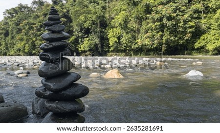 A vertical stack of river stones, carefully balanced and symmetrically arranged, set against a flowing stream backdrop—symbolizing harmony, inner peace, and the delicate balance of nature.