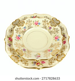 A vertical stack of three antique, fluted fine china plates features a delicate floral pattern, intricate gold filigree trim, and an off-white color, isolated against a bright white background. This overhead shot evokes classic elegance, luxury, and formal dining heritage.