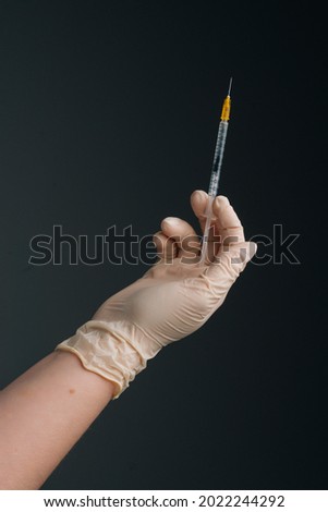 Vertical studio shot of healthcare worker with protective gloves is holding syringe, closeup. Close-up of unrecognizable nurse wearing white latex gloves holding syringe on isolated black background.