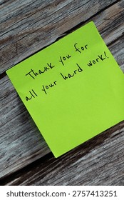Vertical tilted image of one green sticky note that says Thank you for all your hard work, stuck on a wooden surface.
