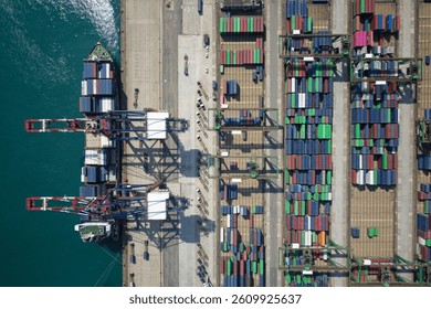 Vertical top down view of cargo containers piled on the quayside and cranes unloading the goods from ships, which are parking at the dock of Taipei Harbor, in Bali District, New Taipei City, Taiwan