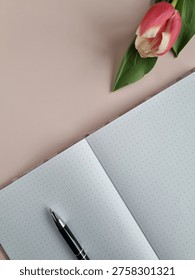 Vertical Top View Open Dotted Notebook, Black Pen And Pink Tulip On Pink Background