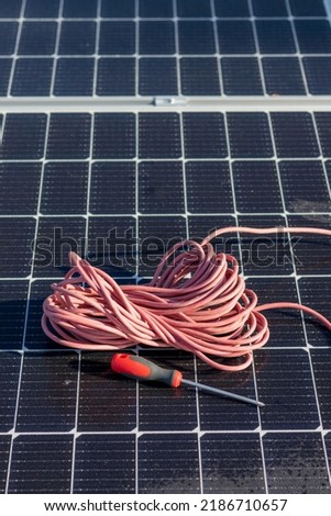 Vertical top view of red cable reel and a screwer leaning on a solar panel installation for renewable energy source