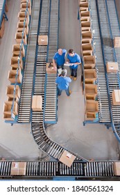 Vertical Top View Of Workers Having A Discussion Among Boxes Laid On Conveyor Belts At A Distribution Warehouse.