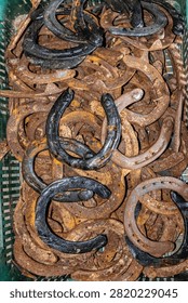 A vertical top-down view of a collection of old rusty metal horseshoes stacked together in a green crate, representing traditional blacksmith craft and lucky charms.