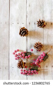 Vertical top-down view of a small group of red frosted cranberries and scattered pinecone ornaments sitting off to the side in the corner of a wood plank backdrop