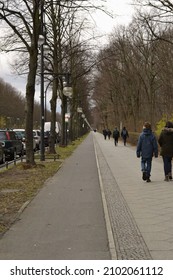 A Vertical Vanishing Point Shot Of A Sidewalk With People And Cars Parked Nearby