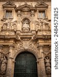 Vertical view of the baroque façade profusely decorated with columns and sculptures of saints of the church of La Merced, next to the university of Murcia, Spain