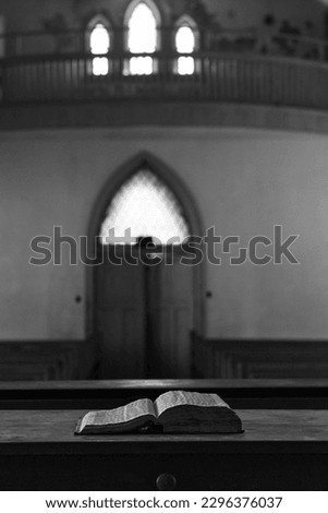 Vertical view of a black and white photo of an abandoned church with bible on the pulpit and arched doorway in the back ground