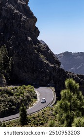 Vertical view of car driving down a challenging mountainous curvy road in the natural area of Roque Nublo, island of Gran Canaria, Canary Islands, Spain. Bird's eye view of a vehicle on lonely drive