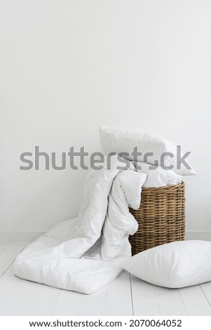 Vertical view of clean bed linen in a wicker basket. Cozy bedroom with white bedding, cotton pillow, sheets and duvet ready for laundry. Household objects in bright interior design at modern apartment