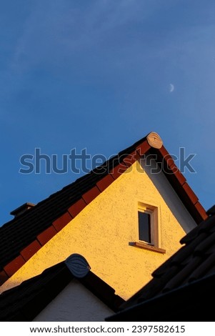 Vertical view of close-up architectural detail of the roof of a residential house with a gable roof, in a small German town. Window feature on the second floor of a sunlit traditional German house