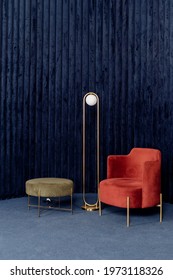 Vertical view of comfortable red armchair, minimalist floor lamp made of metal and pouf or ottoman in cozy room with navy velour walls. Dark blue interior