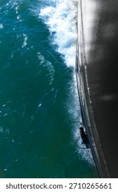 Vertical view down the black bow of a ship in motion towards the splashing water on the hull and anchor