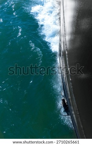 Vertical view down the black bow of a ship in motion towards the splashing water on the hull and anchor