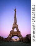 Vertical view of the Eiffel Tower at sunset with a pink and purple gradient sky. Iconic Parisian landmark framed by winter trees and the Champ de Mars park during twilight in France
