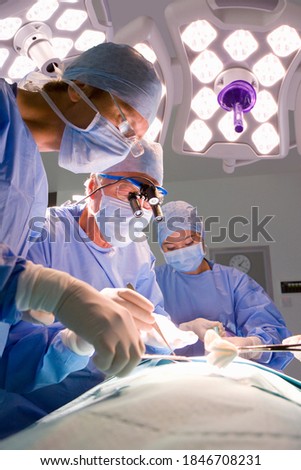 Vertical view of experienced surgeons looking down at the patient while carefully performing the operation in the operating suite
