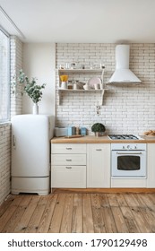 Vertical View Of Fridge, Gas Stove Appliance, Cooking Hood, Built In Oven Equipment, Kitchenware Supplies On Shelves And Green Plants In Kitchen At Modern House With White Interior Design