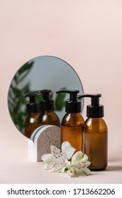 Vertical view of glass bottles with organic and natural cosmetics product near mirror and flower isolated on pastel pink background with copy space