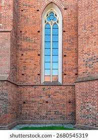 Vertical view of gothic arched window on 14th century brick church built in 1370 in Europe. Historic religious architecture with medieval craftsmanship.