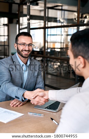 Vertical view of happy businessman in formalwear sitting behind table in office, shaking hands with new employee after good interview