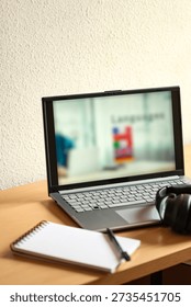 Vertical view of a home study desk representing language learning and lifelong education. Laptop, headphones, blank notebook and pen on a workspace with copy space and shallow depth of field.