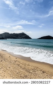 Vertical view of La Concha beach in San Sebastian, Basque Country. Soft overcast light over turquoise bay with Monte Igueldo hill and Santa Clara Island in background.