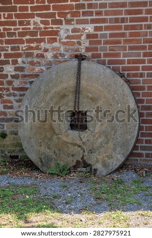 Vertical view of a large old millstone leaning against a red brick wall in Germany
