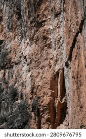 Vertical view of a massive orange and brown limestone cliff face along the Chulilla hiking trail near Valencia, Spain.
