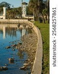 Vertical View north from Sunset Park in Saint Petersburg, Florida with a leading line of seawall with stones, grass and palm trees on right. Central Avenue Bridge on left. Late afternoon sun reflectio