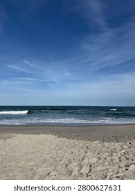 Vertical View Of Ocean Waves Breaking On Sandy Beach Under Sunny Blue Sky