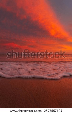 A vertical view of ocean waves hitting a sandy beach during sunset