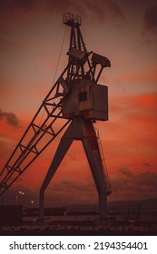 The Vertical View Of An Old Construction Crane Machine Against The Red Cloudy Sky In Wellington Harbor