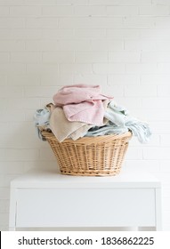 Vertical view of pink towel and blue sheets in wicker laundry basket on white table against painted brick wall (selective focus)
