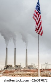 Vertical View Of Smoking Smoke Stacks Of A Generating Station At The Navajo Reservation, Arizona, USA. Smog And Air Polluting Power Plant In The Background, United States Flag In The Foreground.