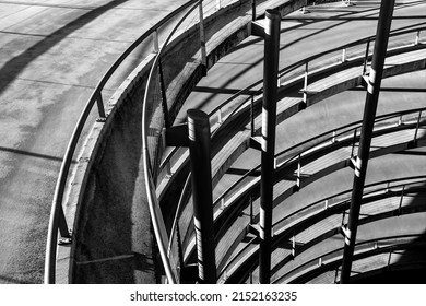 Vertical view of the spiral ascent ramp driveway of big car park in Cologne Germany. Infrastructure building with steel and concrete construction illuminated by sunlight, black and white greyscale. - Shutterstock ID 2152163235