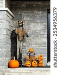 Vertical view of spooky Halloween decorations in porch, including a skeleton dressed in rags, pumpkin scarecrow and other carved squashes, Quebec City, Quebec, Canada