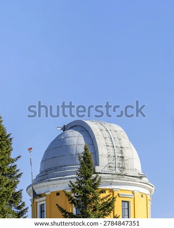 Vertical view of telescope dome tower at Pulkovo Astronomical Observatory in Saint Petersburg, Russia. Historic astronomy building with trees and clear blue sky
