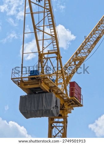 Vertical View of a Yellow Construction Crane and Counterweight Against a Bright Blue Sky with Scattered White Clouds.