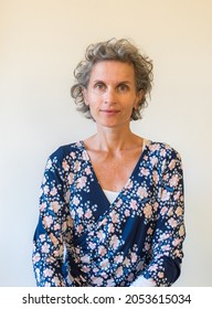 Vertical Waist Up View Of Middle Aged Woman In Blue Floral Dress Against Neutral Background (selective Focus)